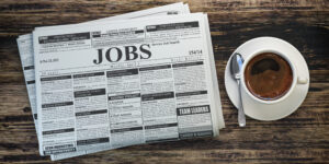job classifieds ads newspaper and coffee cup on wooden table. jo