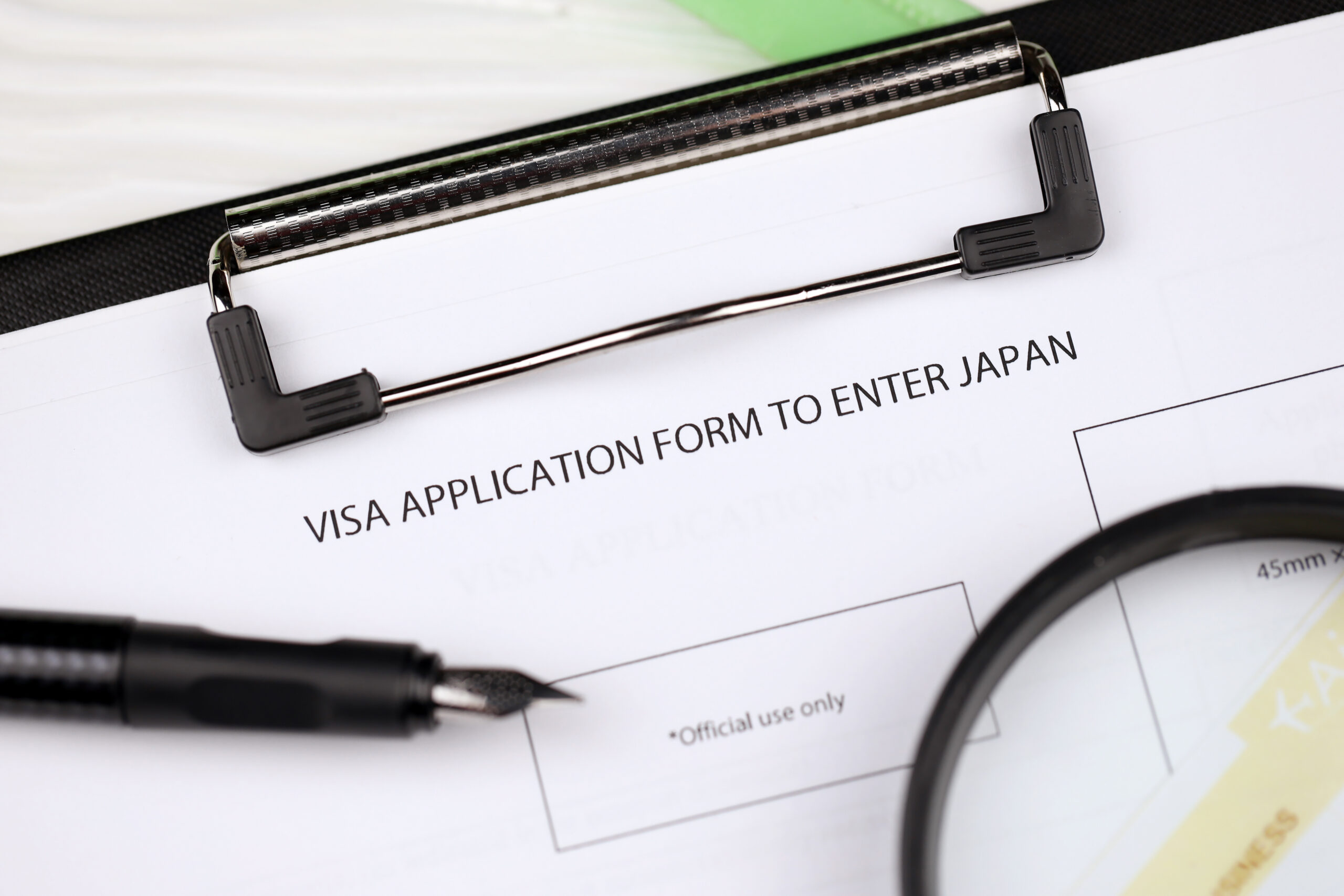 What Happens If Your Residence Card Expires While You're in Japan? visa application to enter japan on a4 tablet lies on office table with pen and magnifying glass