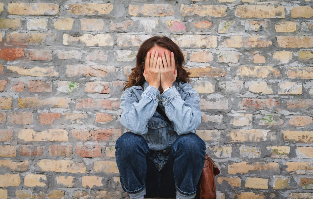 What to Do If Your Rental Application Is Rejected in Japan woman sitting outdoors next to a brick wall, covering her face with her hands in a gesture of distress or sadness.